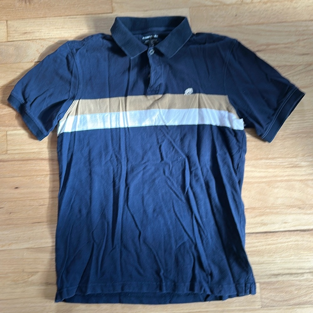 Men’s navy blue polo with tan and white stripe. Elephant emblem on chest.
